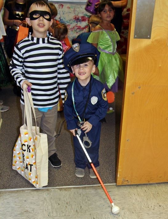 Two children dressed in costumes: a police officer with a white cane and a robber.
